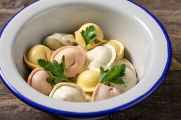 Traditional Russian dumplings made from multi-colored dough. Dumplings on a wooden board in an enamel plate. Cooking concept.