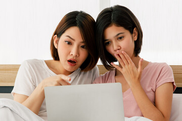 Couple adults lesbians asian women very pretty with short hair look like to surprised and excited for seeing something in her laptop on bed and in room on morning