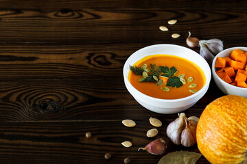 Vegetarian pumpkin cream soup in a white bowl decorated with seeds and herbs on a light background