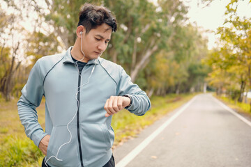 Happy sport man in earphone listen music standing and looking at smartwatch during training and running in the park.