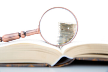 The opened book, the magnifying glass on the book and the coins observed in the magnifying glass