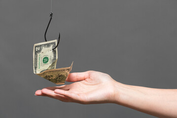 Dollar banknote hanging on the fishing hook and female hand on the gray background. Financial trap...