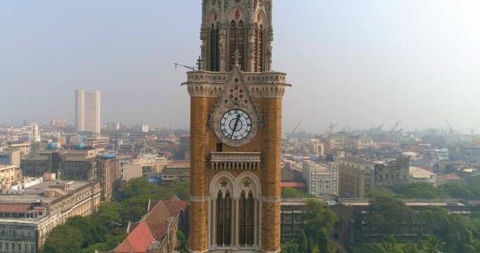 Drone shot of the Rajabai Clock Tower next to the Bombay High Court Building and Oval Maidan, an ornate 1878 clock tower modeled after Big Ben and featuring stained-glass windows and musical chimes