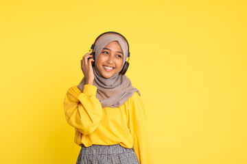 attractive asian woman listening music on yellow background. Woman wearing headset.