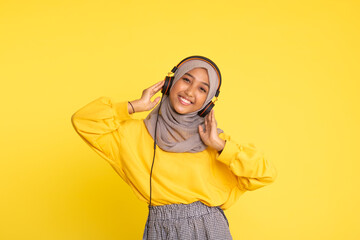 attractive asian woman listening music on yellow background. Woman wearing headset.