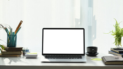 Front view of computer laptop, notebook, coffee cup and plant on white desk at modern home office.