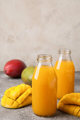 Bottles of fresh mango juice on grey background