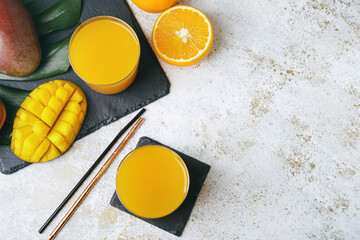 Glasses of mango juice and tropical fruits on light background