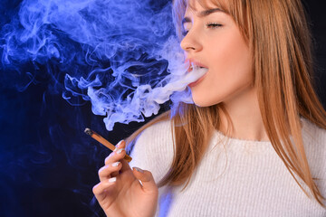 Fototapeta premium Young woman with cigarette on dark background