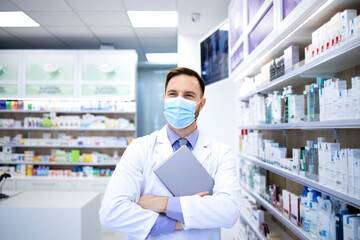 Portrait of pharmacist in protection mask holding tablet computer and standing in pharmacy shop.