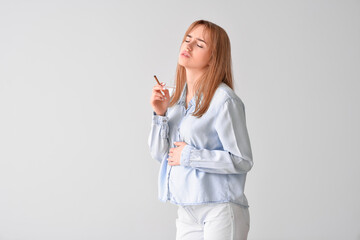 Sick pregnant woman with cigarette on grey background