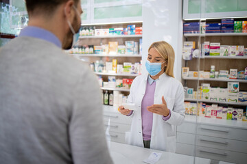 Vrouwelijke apotheker die vitamines en medicijnen verkoopt aan de klant in de apotheek tijdens een pandemie van het coronavirus.