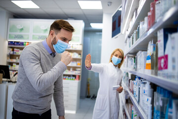 Pharmacist stepping back while sick customer coughing and spreading corona virus in pharmacy shop. Global covid-19 virus pandemic and prevention.
