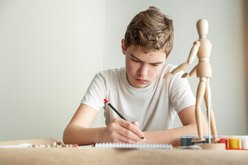 A teenage Caucasian boy learns to draw. A boy draws a man on a model. Creative hobby. Drawing lesson.