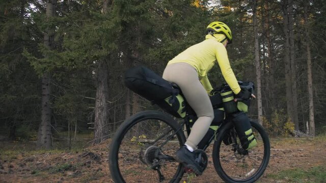 The woman travel on mixed terrain cycle touring with bike bikepacking outdoor. The traveler journey with bicycle bags. Stylish bikepacking, bike, sportswear in green black colors. Magic forest park.
