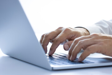 Hands of a man with white shirt typing on a laptop or notebook computer on a desktop while working in the office using internet, input data for information analysis and sending an email message.
