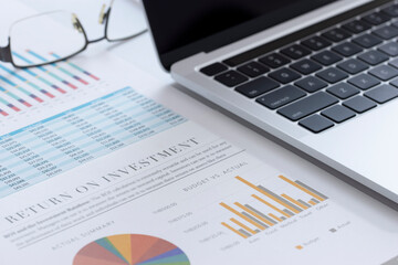 Closeup of laptop or notebook computer and financial reports with colorful charts, graphs and diagrams for business performace and return on investment, ROI, analysis
