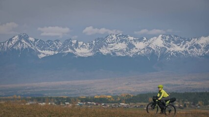 The woman travel on mixed terrain cycle touring with bikepacking. The traveler journey with bicycle bags. Sport tourism bikepacking, bike, sportswear in green black colors. Mountain snow capped.