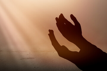 Silhouette of Muslim man standing while raised hands and praying