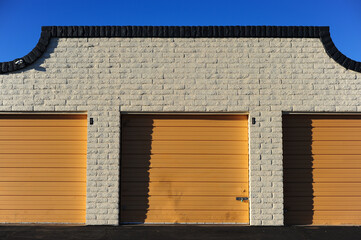 Row of closed orange roll-up doors on brick self-storage facility, illustrating commercial storage unit infrastructure and secure property rental operations
