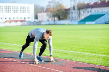 Young runner man in starting position ready for running on the stadium racetrack. Fit male athlete...
