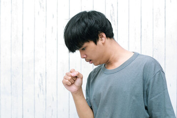 Asian young man feeling unwell and coughing as symptom for cold or bronchitis