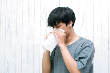 Young asian man sneezing in tissue paper at home