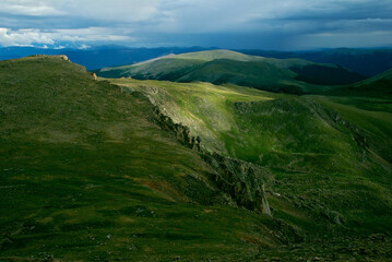 Obraz premium A spot of sunlight on a mountain ridge highlighting the green rocky tundra with a panoramic view of the surrounding mountains in the background. View from Mt. Evans Highway Colorado USA