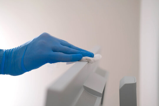 A Male Hand In Rubber Gloves Wipes The Dust From A Computer Monitor With A Napkin. Disinfection At Home, Cleaning In The Context Of The COVID-19 Pandemic.