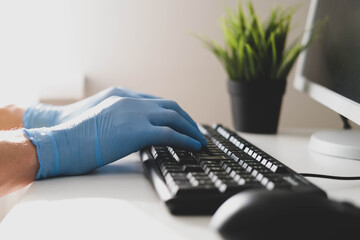 Male hands in blue nitrile gloves use the keyboard on the computer, do the work. Office work in the...