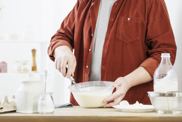 Fototapeta na wymiar middle-aged man kneading pancake dough on white kitchen