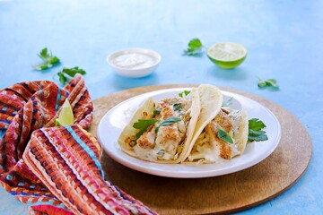 Tacos with chicken, cabbage salad and sour cream sauce in a wheat tortilla on a white plate on a blue concrete background.