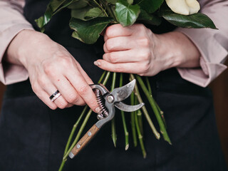 A florist makes a composition, a flower girl with a pruner in her hand, collects a bouquet of roses.