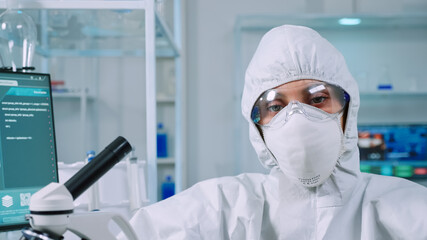 Professional woman scientist in protection suit looking tired at camera in equipped lab. Overworked team examining virus evolution using high tech and tools for scientific research vaccine development