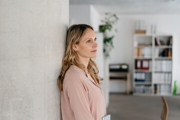 Thoughtful young business woman relaxing against an interior pillar