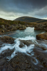 waterfall with silky water towards mountain with cloudy sky. tourism and travel concept- Fairy Pools - Skye Island - Scotland - Uk