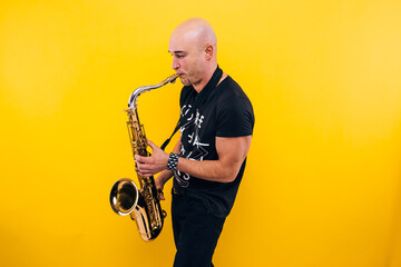 Man plays the saxophone in the studio on a yellow background