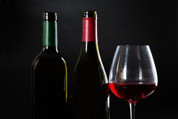 several different bottles of wine and a glass with red wine on a dark glossy background.