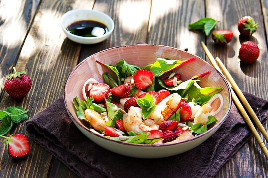 Salad with fresh strawberries, fried shrimp and young beet tops in a pink bowl