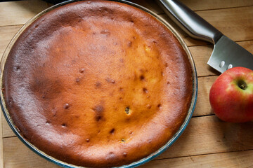 Golden brown fresh home made cake in a glass mould next to a knife and apples