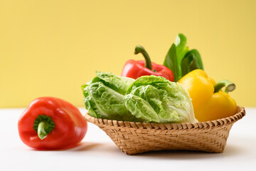 Fresh cos lettuce and bell peppers in a basket on white and yellow background