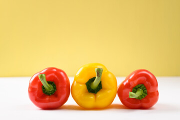 Fresh red and yellow bell peppers on white and yellow background