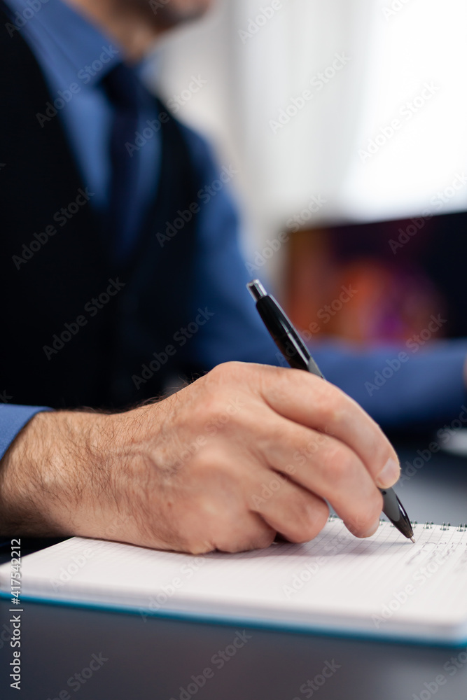 Poster close up of man taking notes on notebook while working from home. elderly man entrepreneur in home w