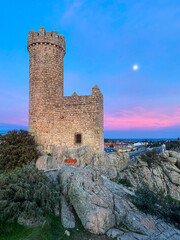 Medieval castle with full moon and colorful sunset in the background.
