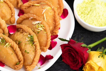 Delicious Gujia Or Gujiya Mithai Made In Desi Ghee Dry Fruits Pista Badam Kesar Is Enjoyed On Festivals Like Happy Holi Diwali Rakshabandhan Deepawali Eid. Rose Flower Decoration On Black Background