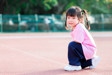 A 3-4 years old Asian girl pretends to run on a treadmill. Cute children exercise outdoors in summer. Happy child wore a pink shirt.