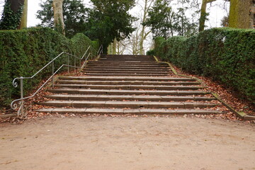 old stone stairs in the park with metal railings and surrounded by green hedges