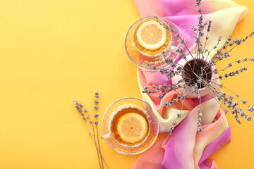 Two cups of tea with a light napkin and a bouquet of lavender on a yellow background, space for text, top view