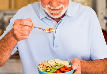 Smiling elderly man holding a bowl of fresh and dried fruits. Breakfast or lunch time, healthy...