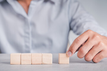 Businessman wearing a blue shirt, arranging the empty wooden blocks with his hands. Which is placed on a white wooden table. Business strategy and action plan. Copy space.